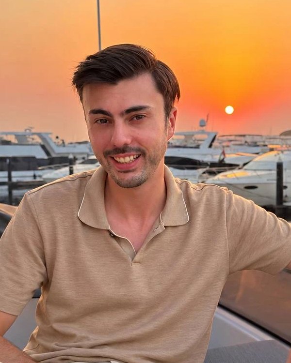 Joe Grech, founder of Dusk Studios, smiling on a boat at a marina at sunset
